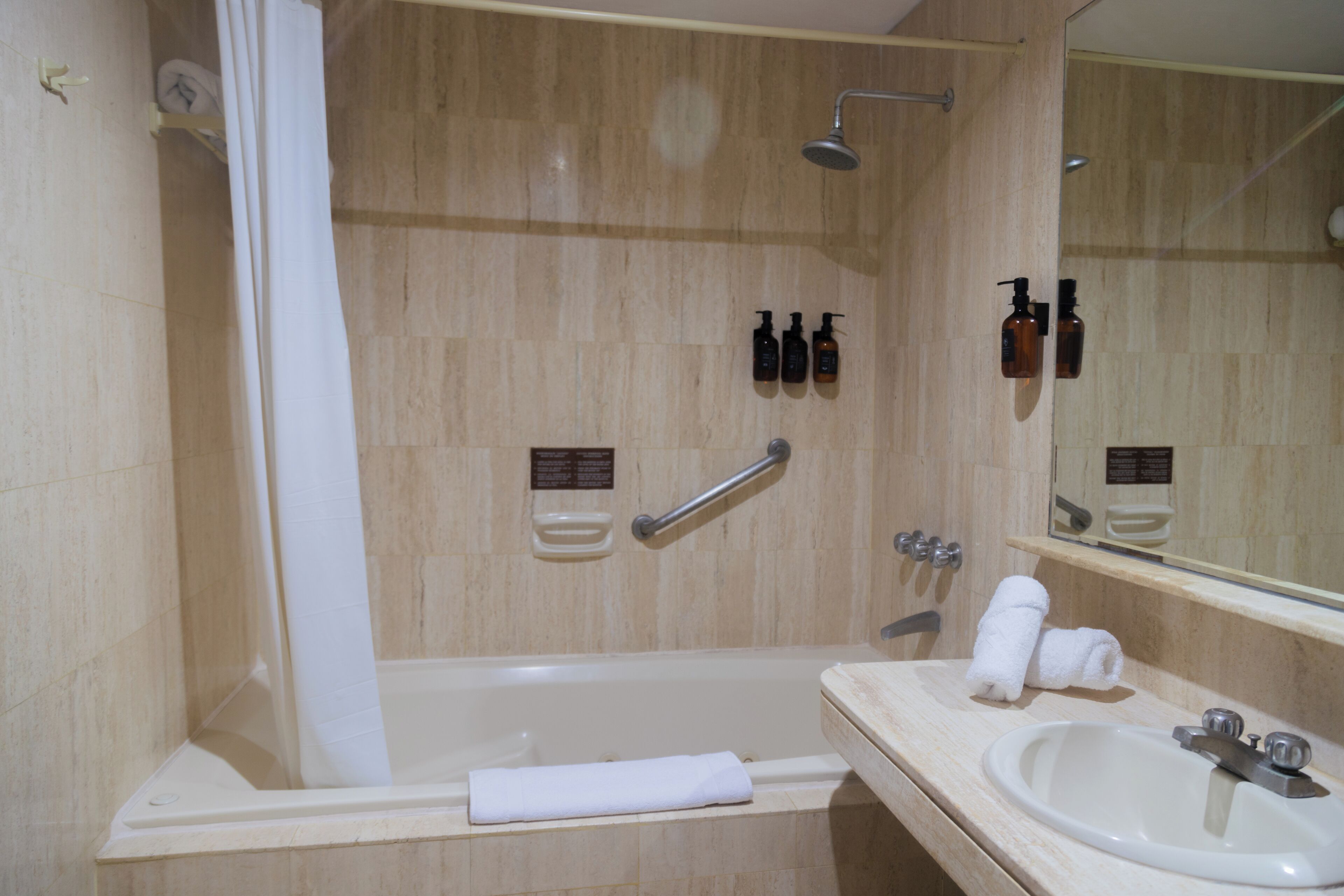 A bathroom with a bathtub, a sink, and a mirror. There are toiletries on the wall and a towel on the floor.