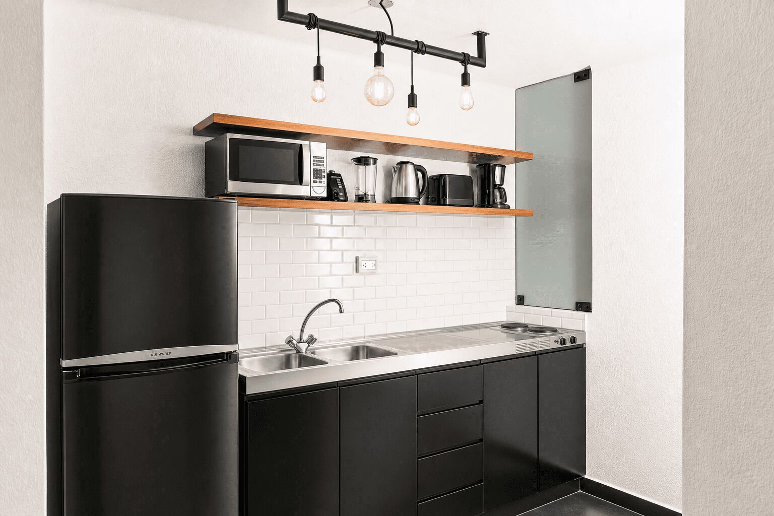 A modern kitchen with a black refrigerator, stainless steel sink, and a microwave on a wooden shelf.