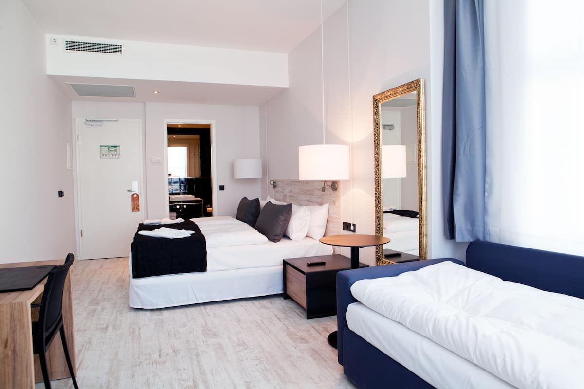 A hotel room with two beds, a desk, a chair, a lamp, and a mirror.