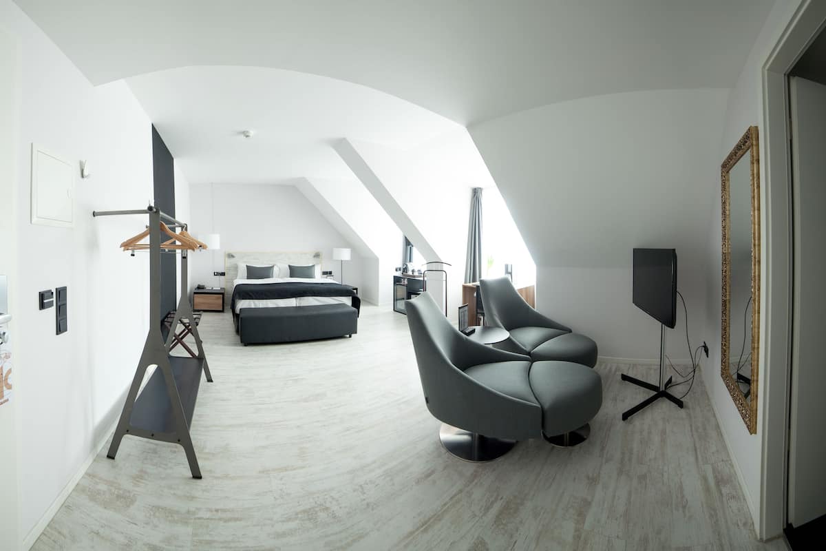 A modern hotel room with a loft bed, a grey armchair, a flat-screen TV, and a large mirror.