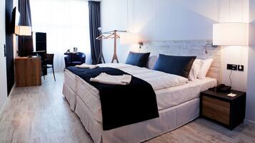 Hotellihuone, jossa on sänky, yöpöytä, lamppu, televisio, työpöytä, tuoli ja näkymä ulos.
