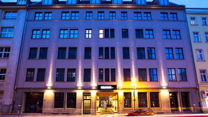 Un hôtel à plusieurs étages, doté d’une entrée centrale, de grandes fenêtres et d’un toit plat.
