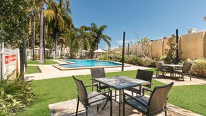 Una zona junto a la piscina con piscina, mobiliario de exterior y césped cuidado.