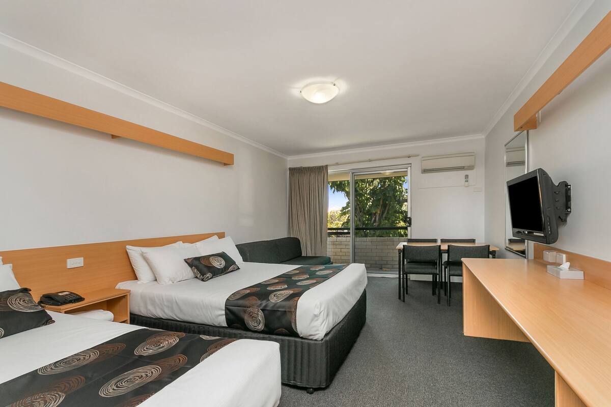 A hotel room with two beds, a desk, a TV, and a balcony with a view.