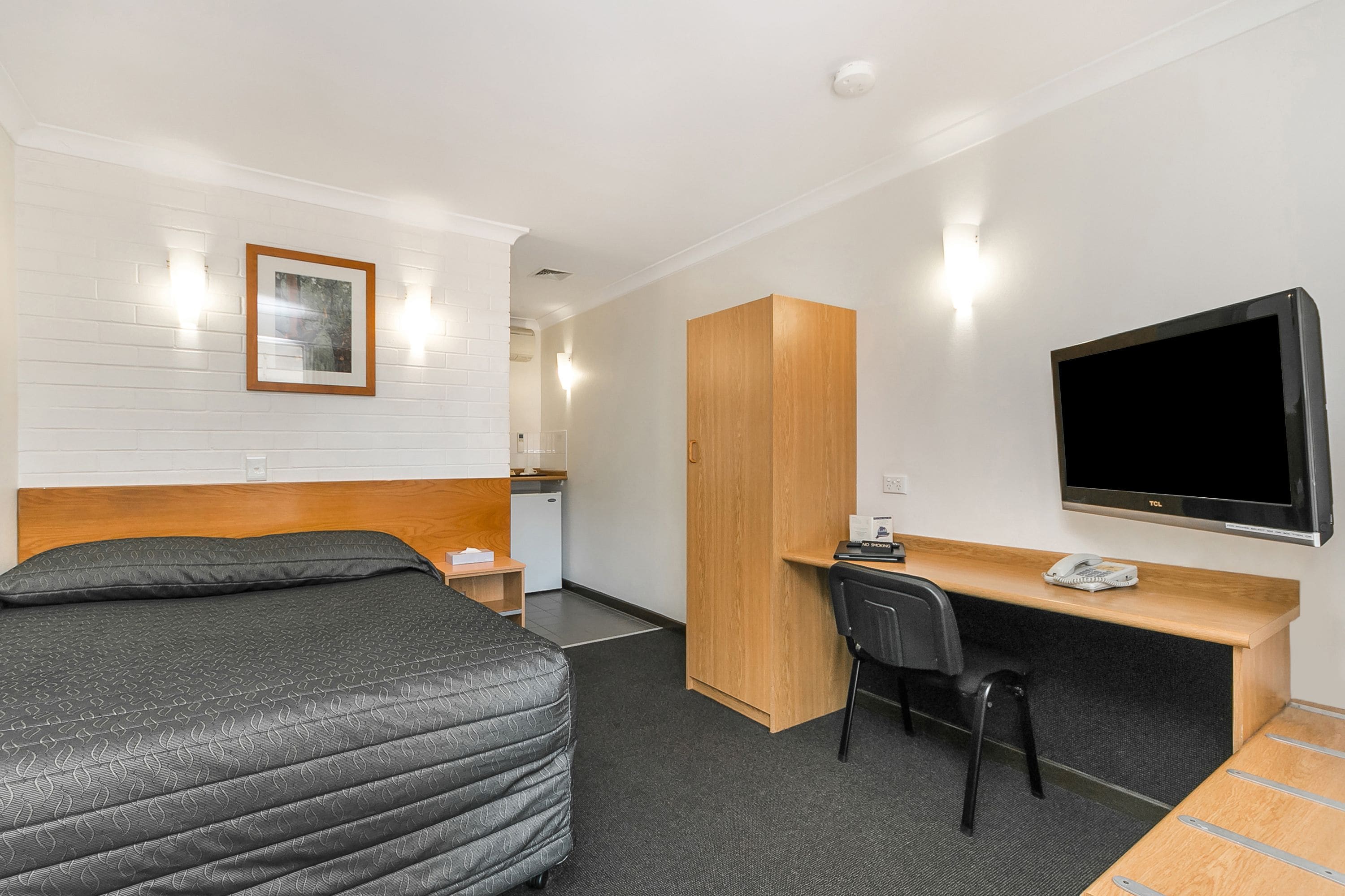 Una habitación de hotel con cama, escritorio, silla, televisor y armario.