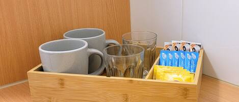 A wooden box containing three gray mugs, two clear glasses, and packets of sugar.