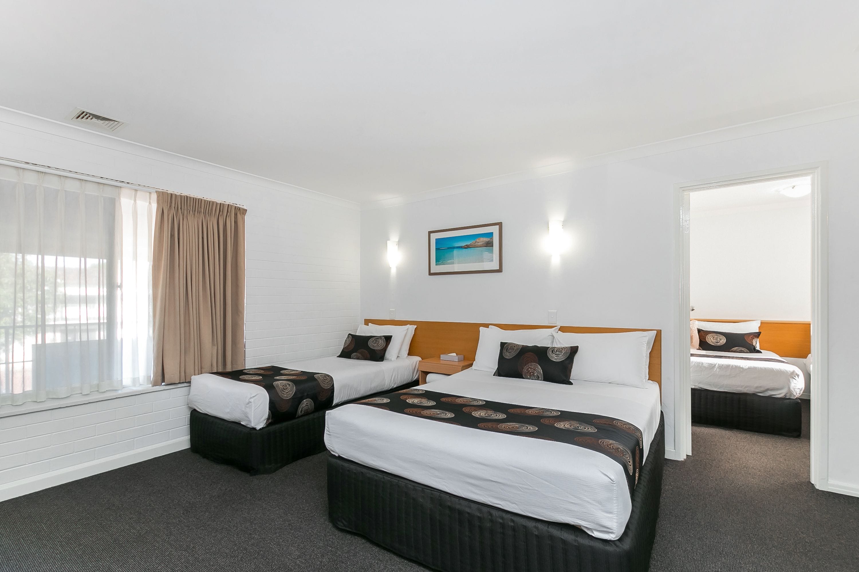 Habitación de hotel con dos camas, un ventanal con cortinas, un cuadro en la pared y suelo alfombrado.