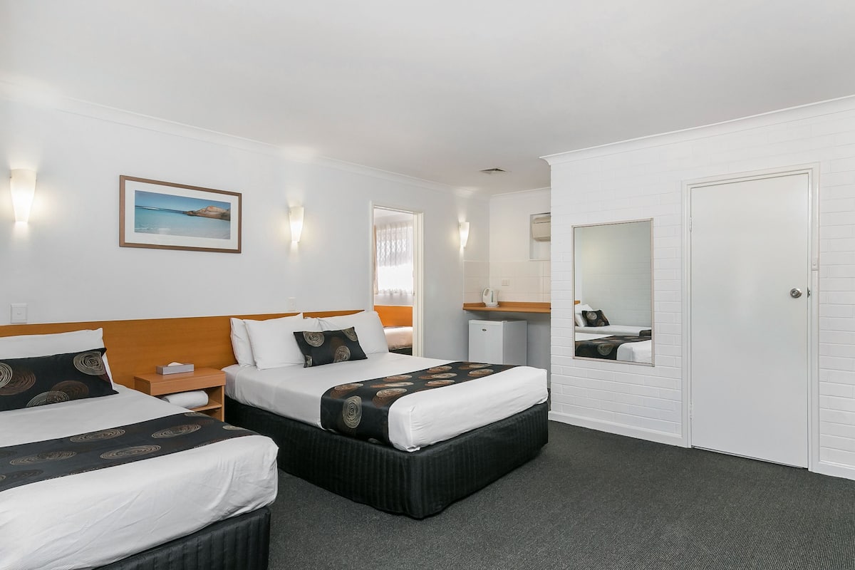 A hotel room with two beds, a small desk, a mirror, and a wardrobe.