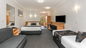 Habitación de hotel con dos camas, un sofá, un escritorio, un televisor y un espejo.