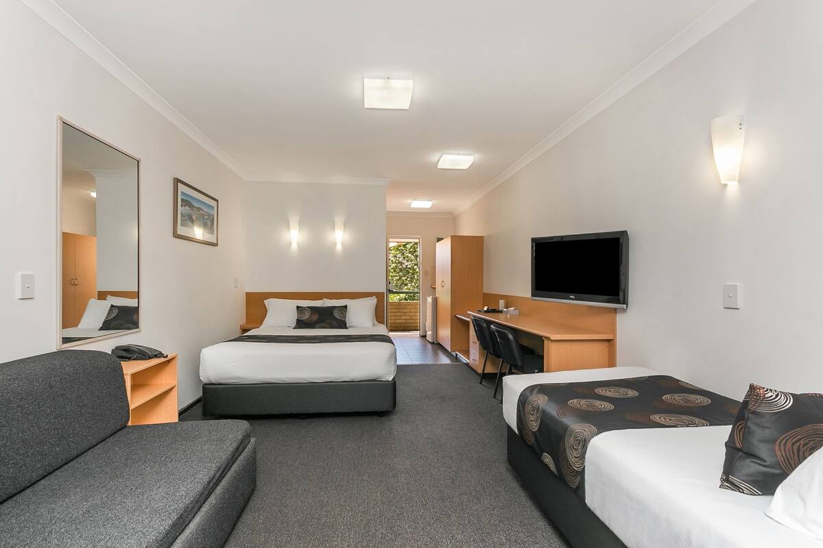 A hotel room with two beds, a sofa, a desk, a TV, and a mirror.