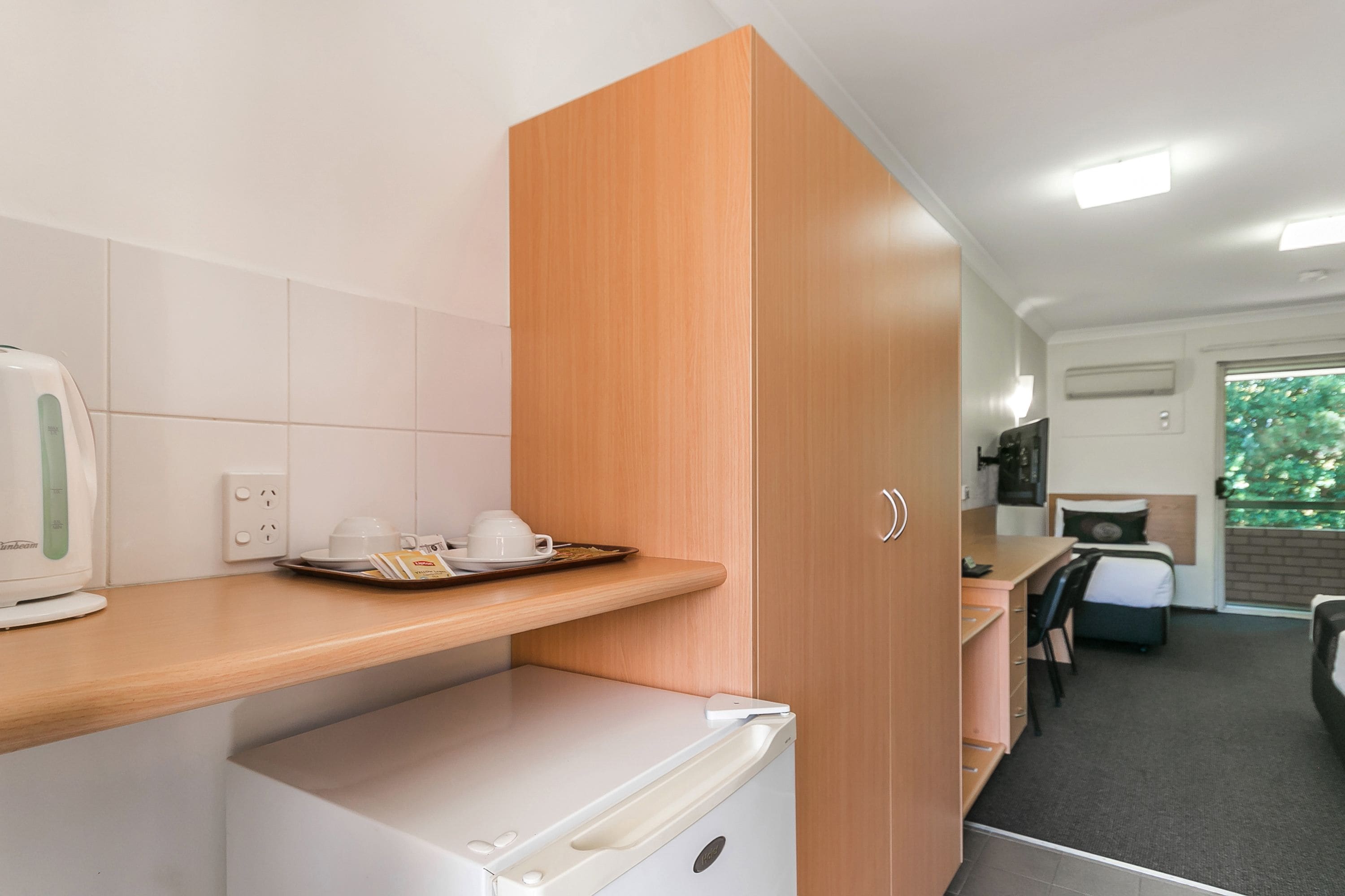 A compact kitchenette with a coffee maker, a small refrigerator, and a breakfast tray on the counter.