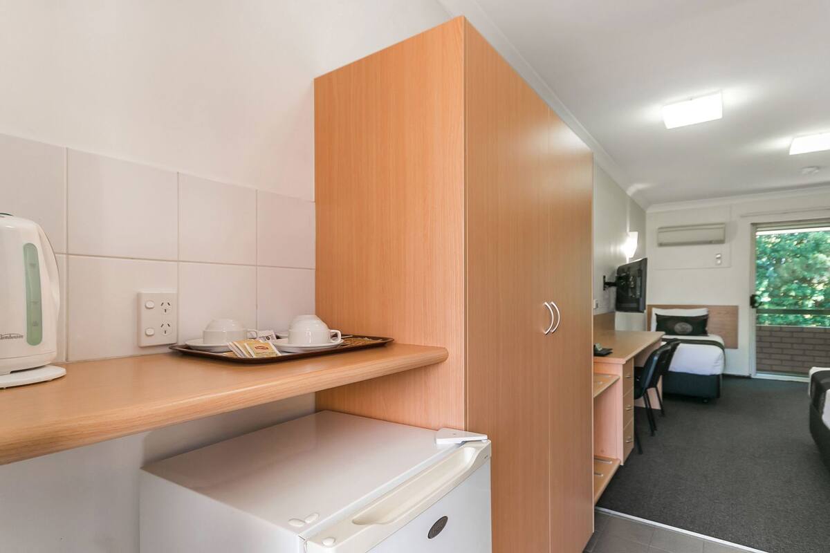 A compact kitchenette with a coffee maker, cups, and a tray of breakfast items.