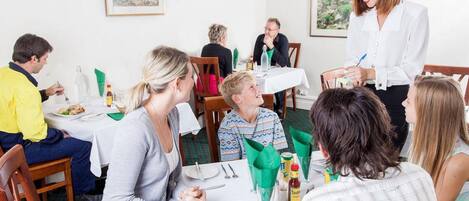 Un espace repas avec des tables dressées pour le service, des chaises et un serveur qui s’occupe des clients.