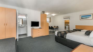 A hotel room with a bed, a desk with a TV, a bathroom, and a dining area.