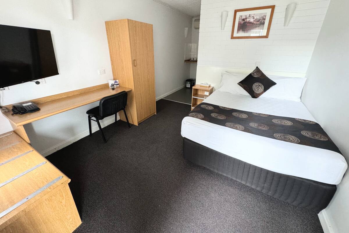 A compact hotel room with a single bed, a desk, a chair, a television, and a small wardrobe.