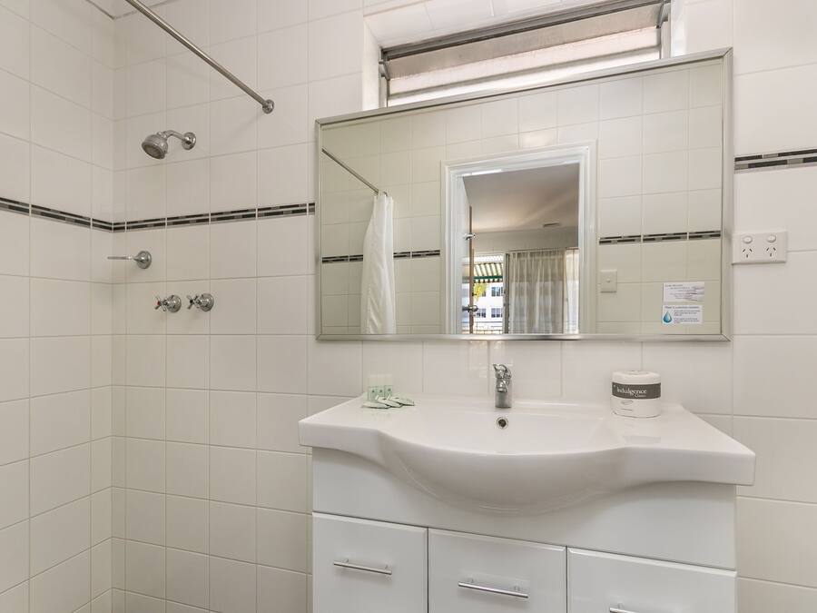 Un baño con azulejos blancos, un lavabo, un espejo, una ducha y un perchero para toallas.