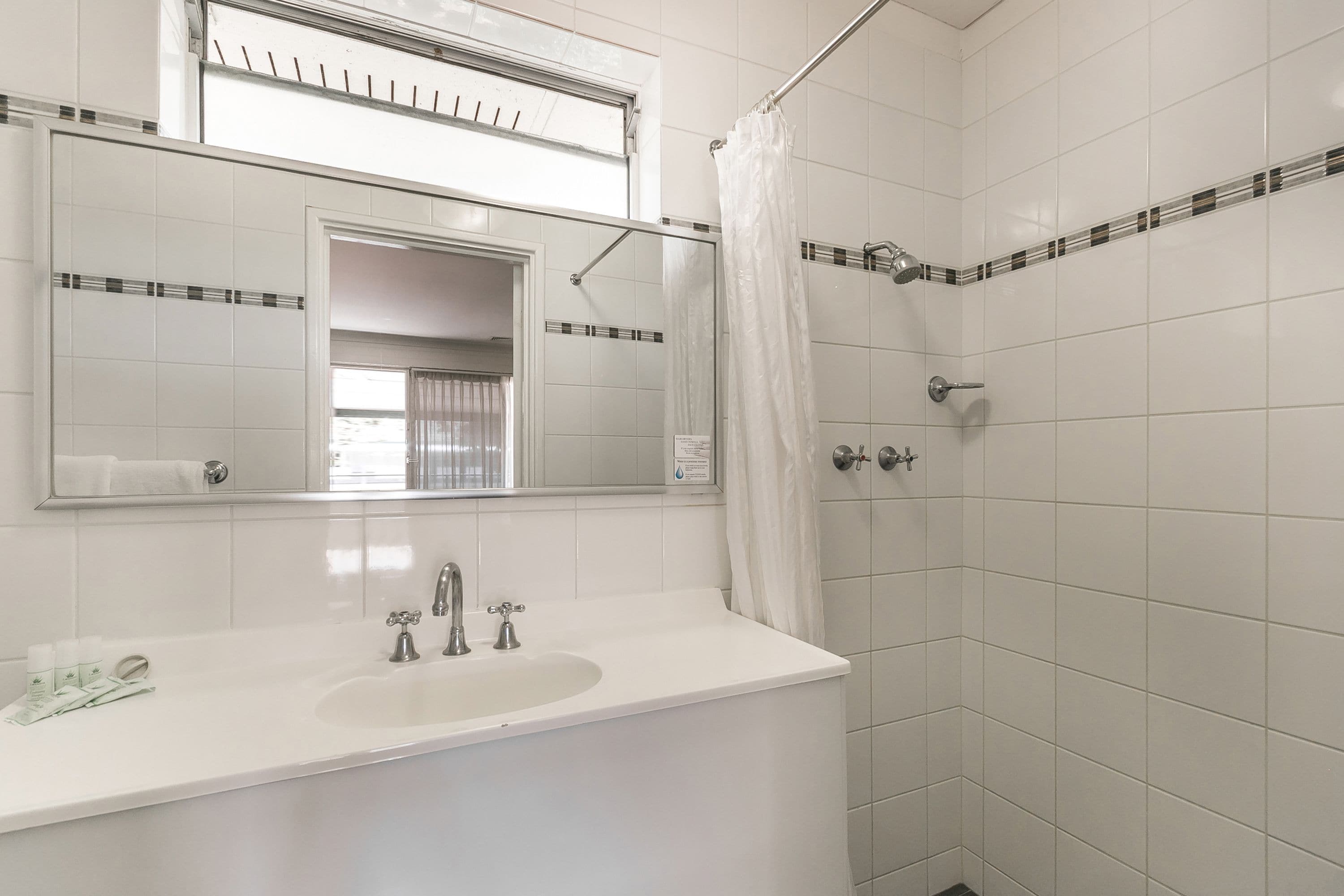 Un baño con un lavabo blanco, dos grifos, un espejo y una ducha con cortina.