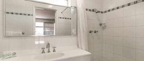 Un baño con un lavabo blanco, dos grifos, un espejo y una ducha con cortina.
