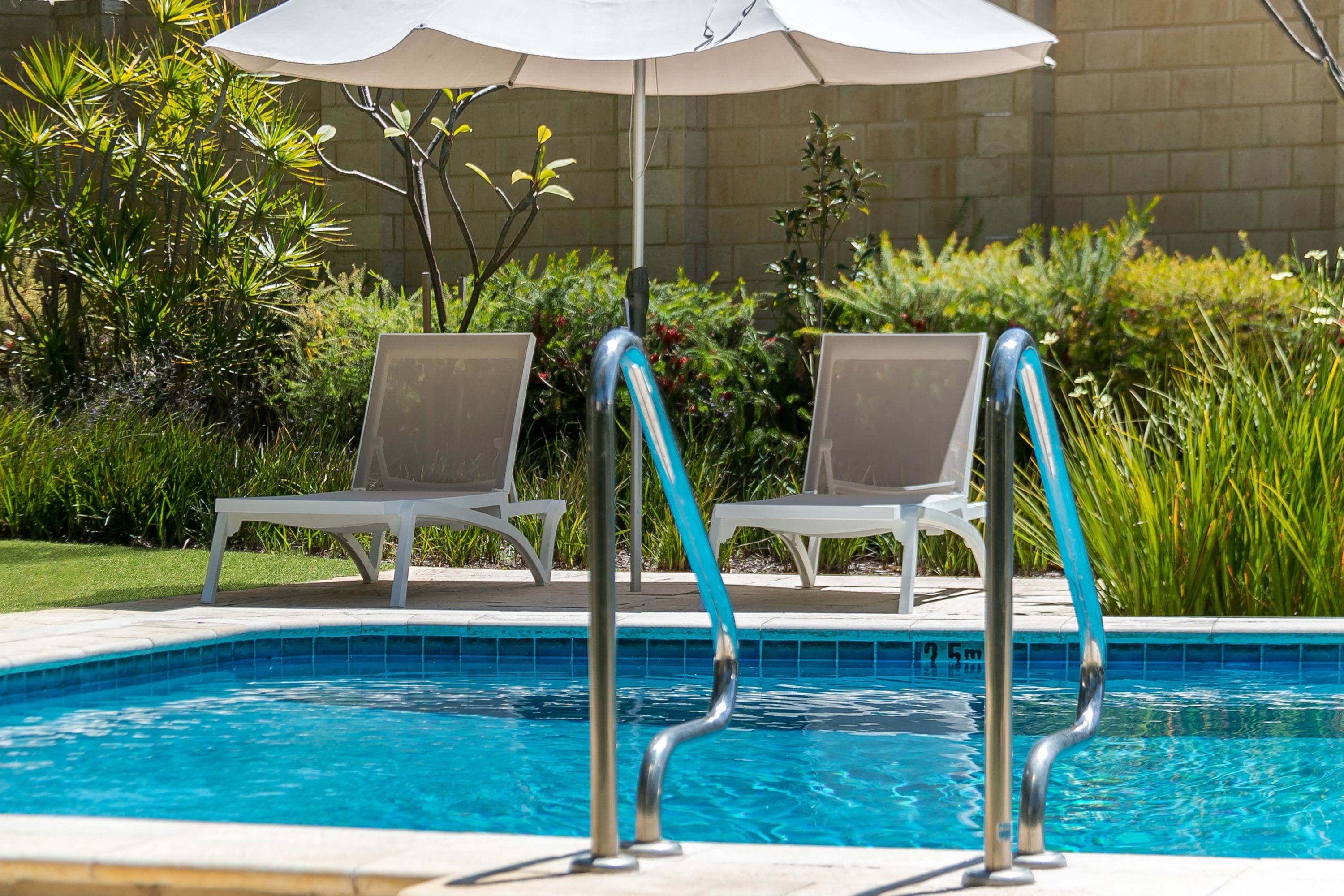 Una piscina con dos sillas de descanso y una sombrilla blanca.