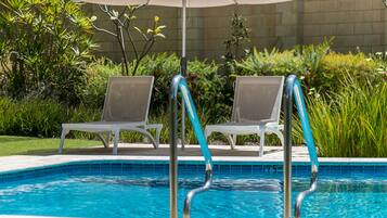 Una piscina con dos sillas de descanso y una sombrilla blanca.
