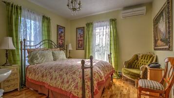Un dormitorio con cama, una silla, cómoda, lámpara y un cuadro en la pared.