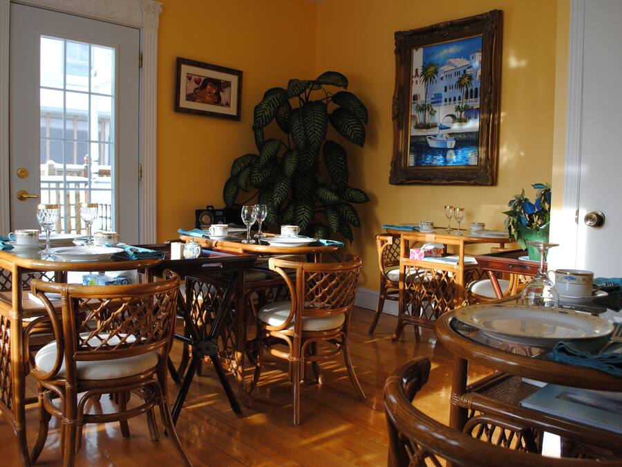A dining area with wooden tables and chairs, a large potted plant, and a painting on the wall.
