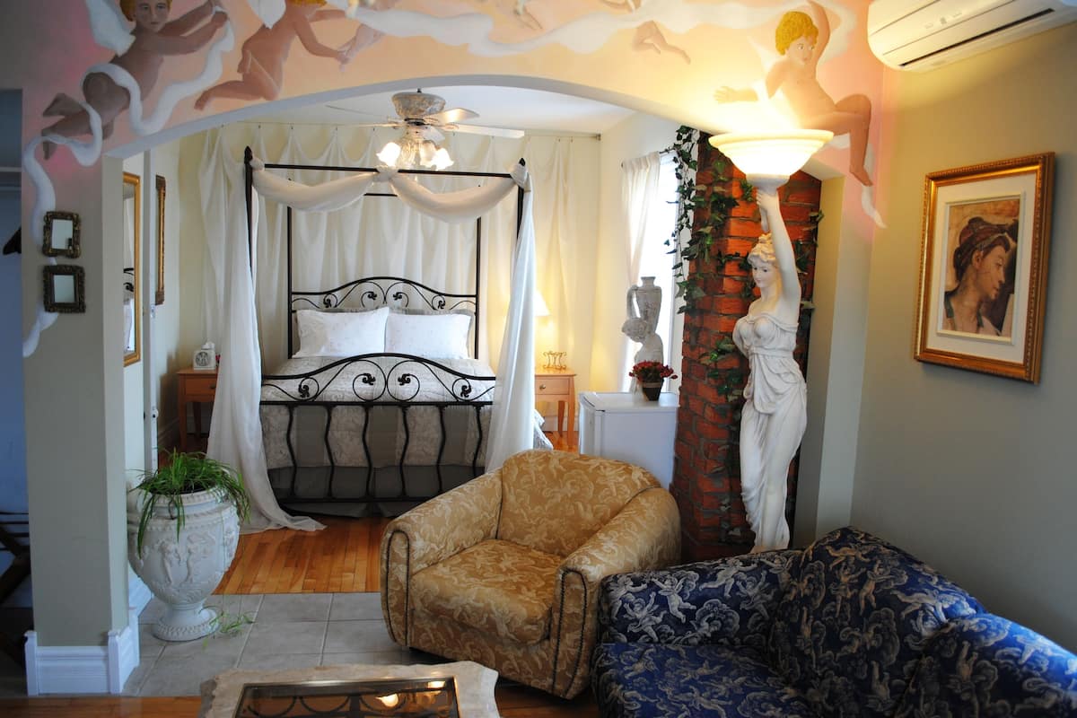 Ein Schlafzimmer mit einem Himmelbett, einer Sitzecke mit Sofa und Sesseln sowie einer dekorativen Decke.