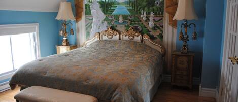 A bedroom with a large bed, a bench, a mural on the wall, and two nightstands with lamps.