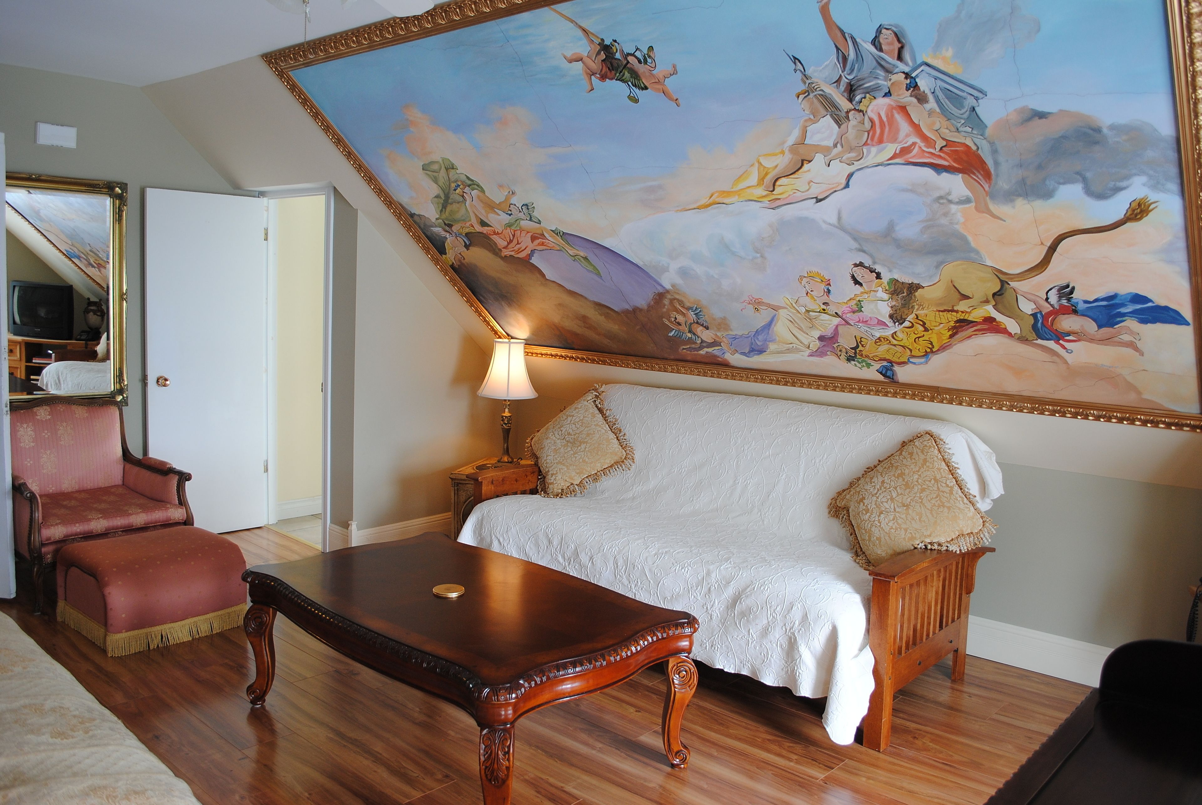 Une pièce avec une grande fresque murale, un canapé, un fauteuil et une table en bois.