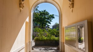 Ein gewölbter Gang mit Blick auf einen Baum und Gebäude im Hintergrund.