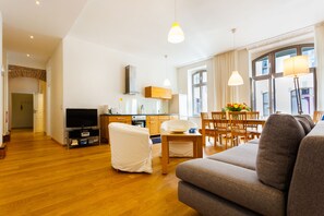 A spacious living room with a sofa, a TV, and a dining area with chairs and a table. - Downtown City Landmark Near Checkpoint Charlie (Berlin)