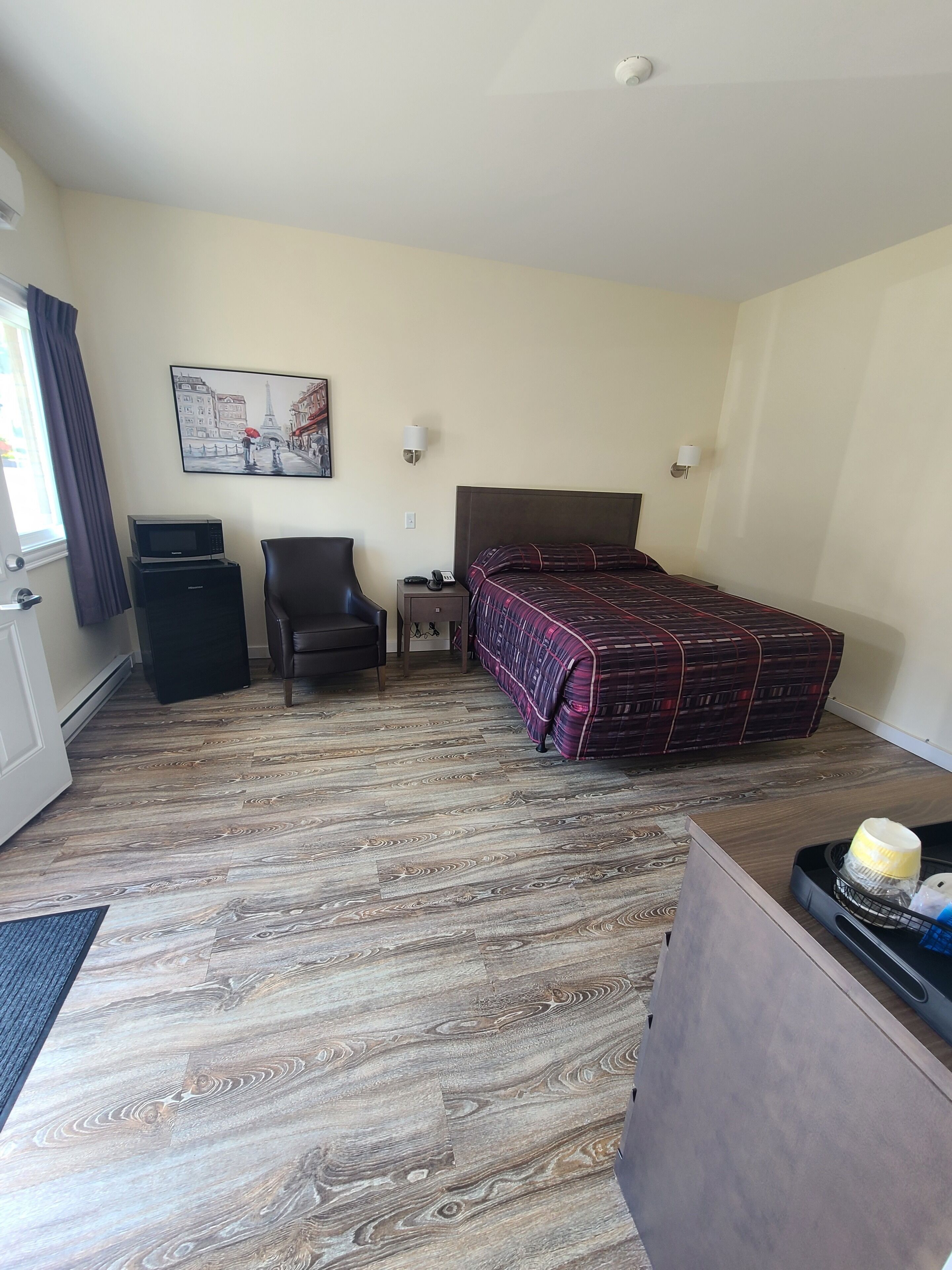 Ett hotellrum med en säng, en stol, ett skrivbord, en mikrovågsugn och en tavla på väggen.