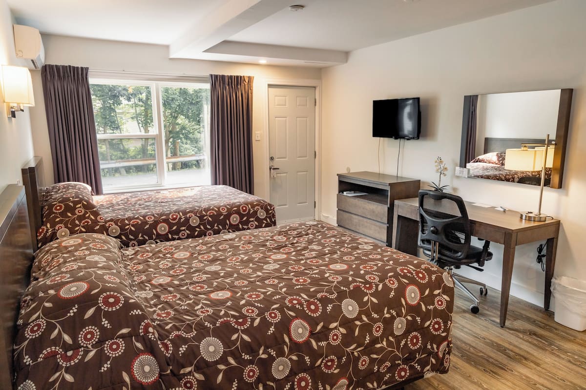 A hotel room with two beds, a desk, a chair, a TV, a mirror, and a window with curtains.