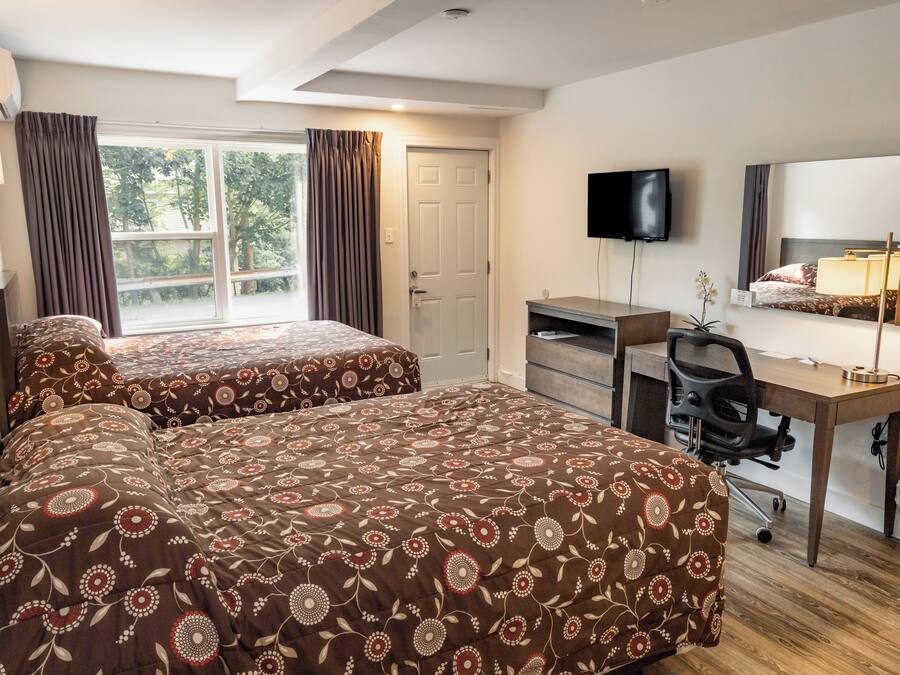 A hotel room with two beds, a desk, a chair, a TV, a mirror, and a window with curtains.