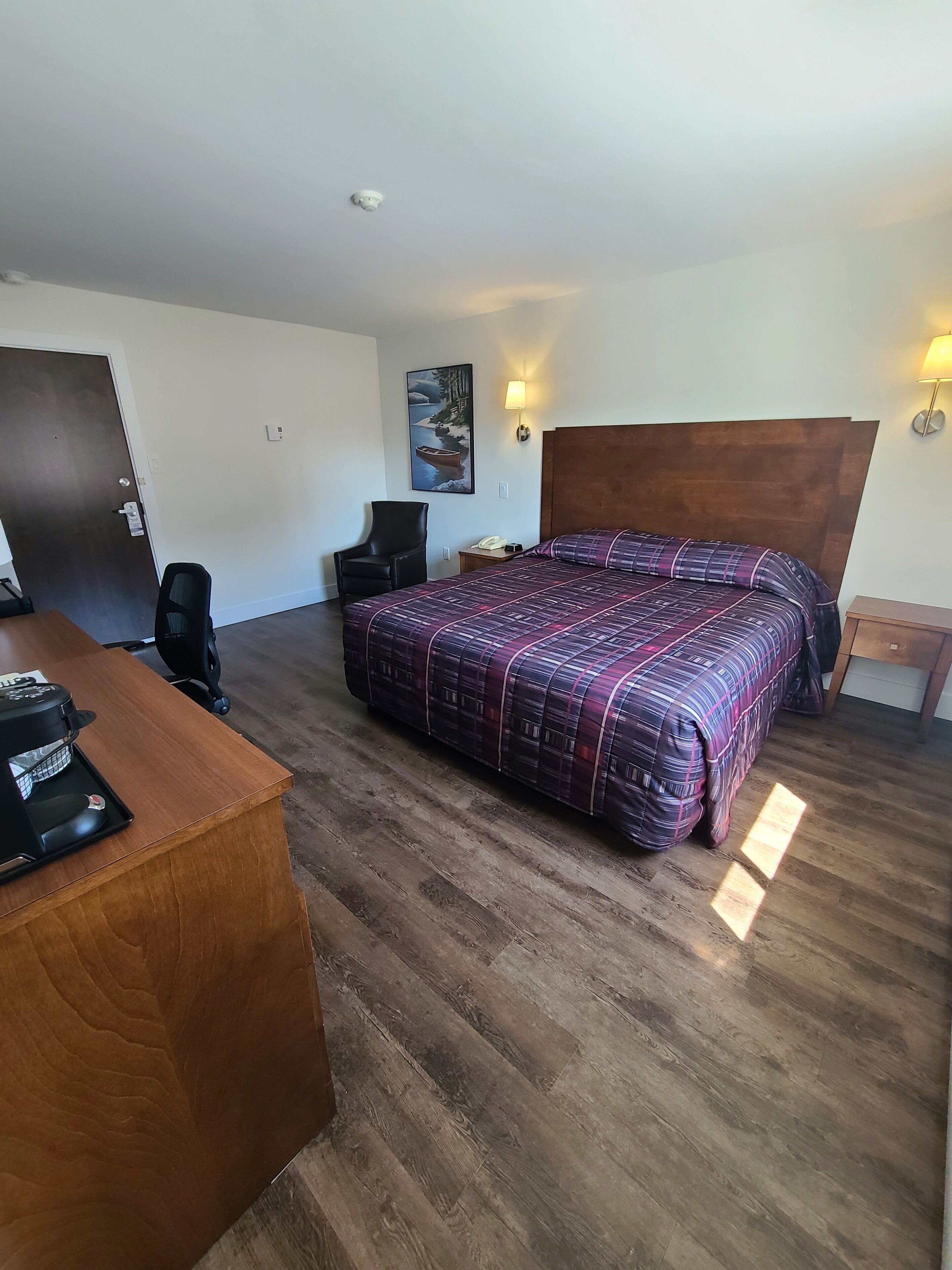 Habitación de hotel con cama, escritorio, silla y suelo de madera.