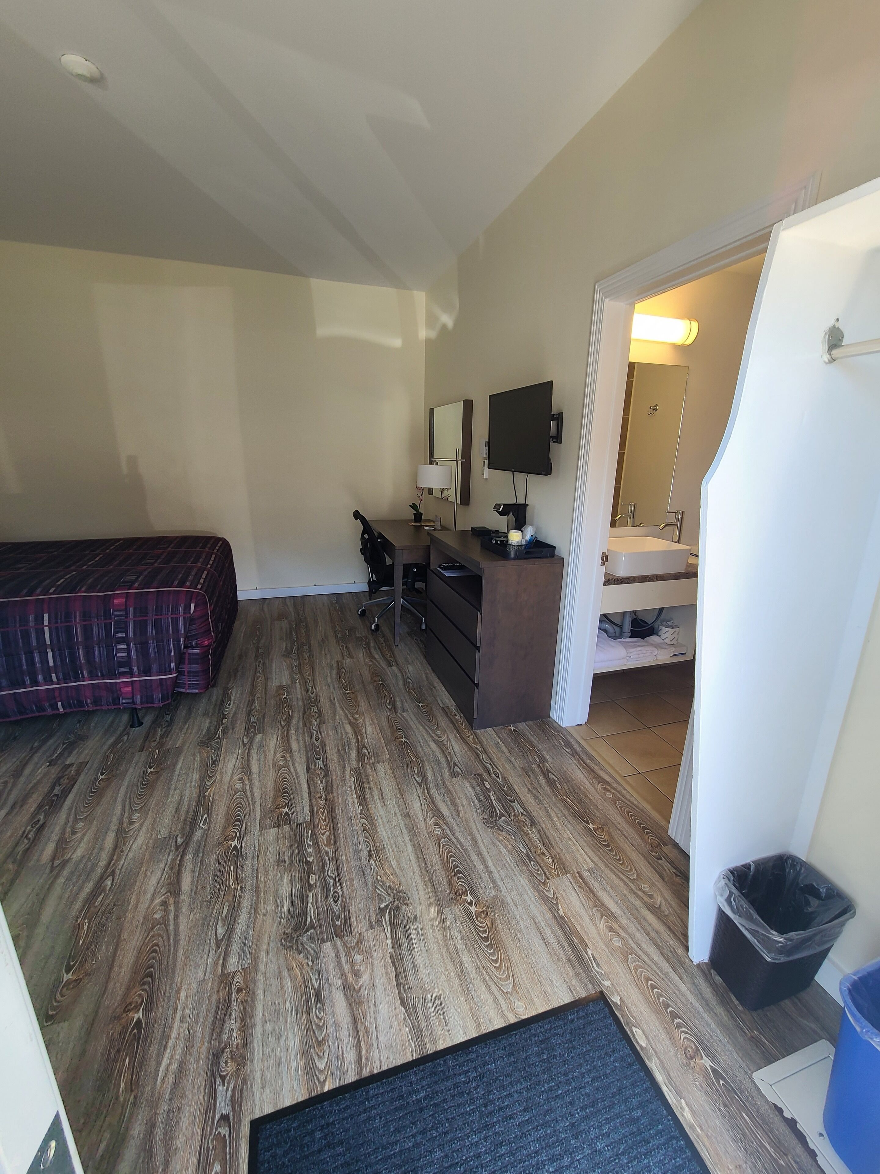 A hotel room with a bed, desk, chair, and a bathroom visible through an open door.