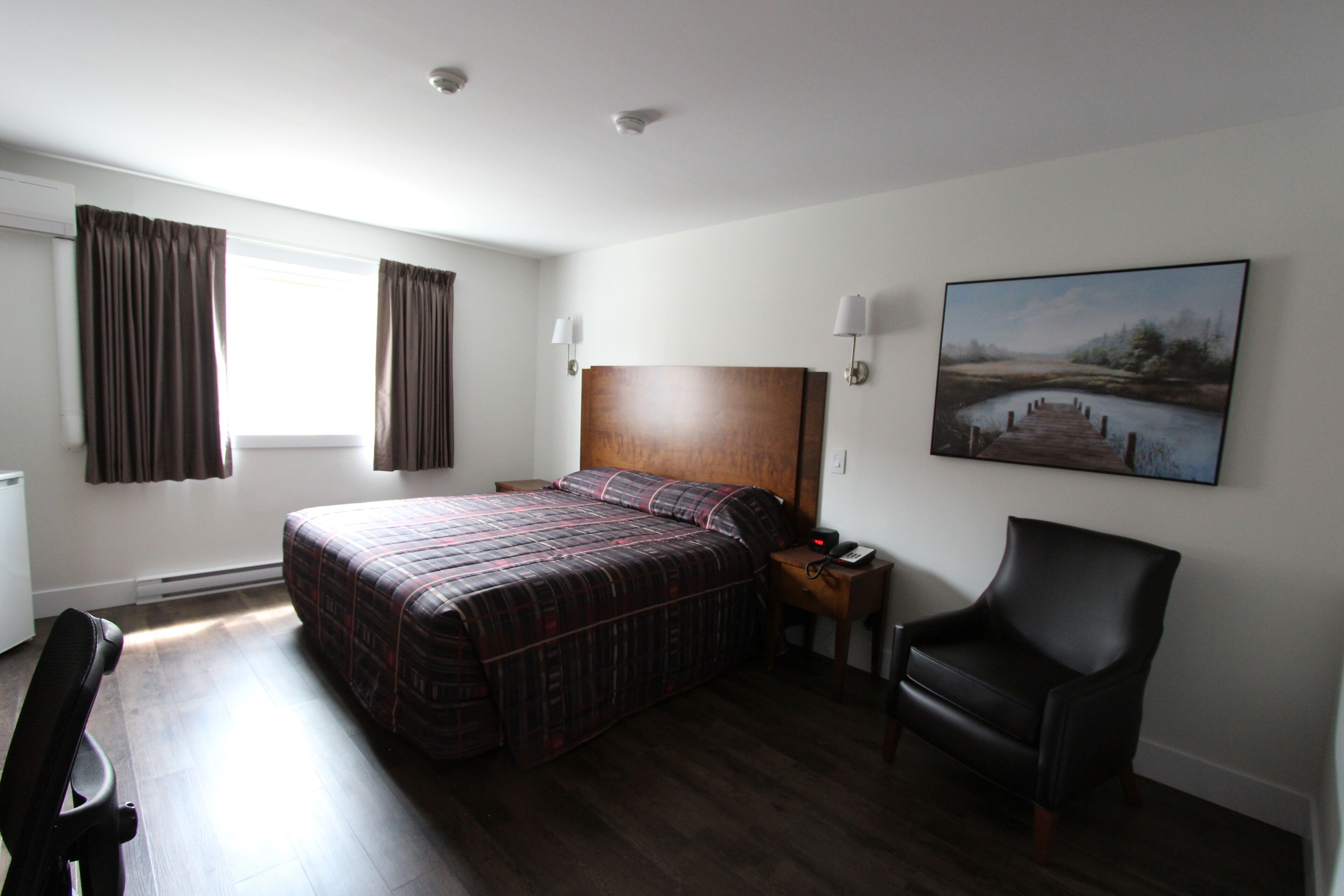 Habitación de hotel con una cama grande, un escritorio, una silla, una mesita de noche y un cuadro en la pared.