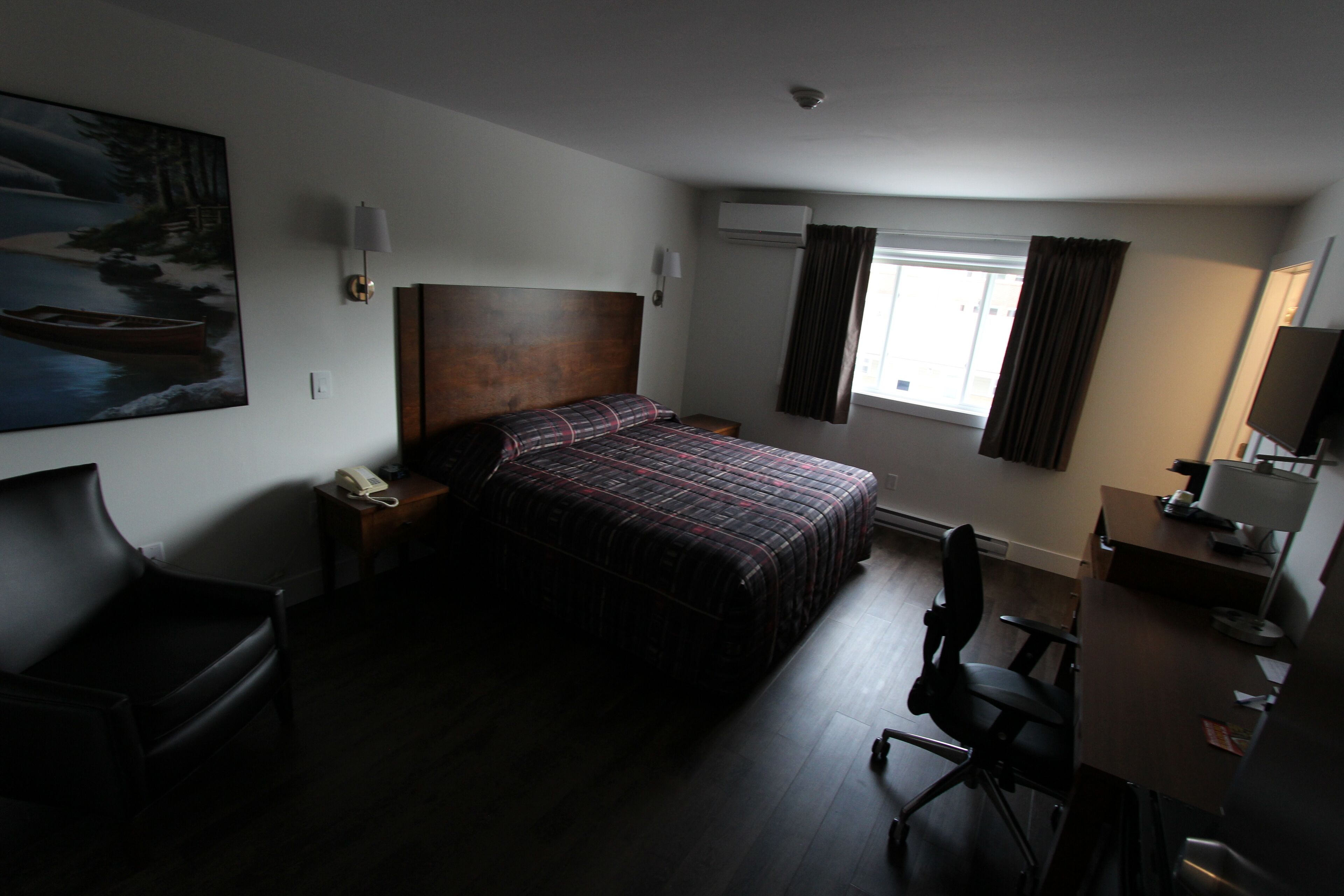 Una habitación de hotel con una cama grande, un escritorio con ordenador, una silla, una lámpara y un cuadro en la pared.