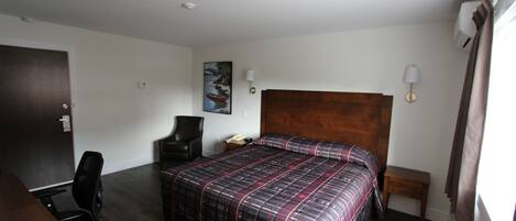 Una habitación de hotel con una cama grande, un escritorio, una silla, una mesita de noche y un cuadro en la pared.