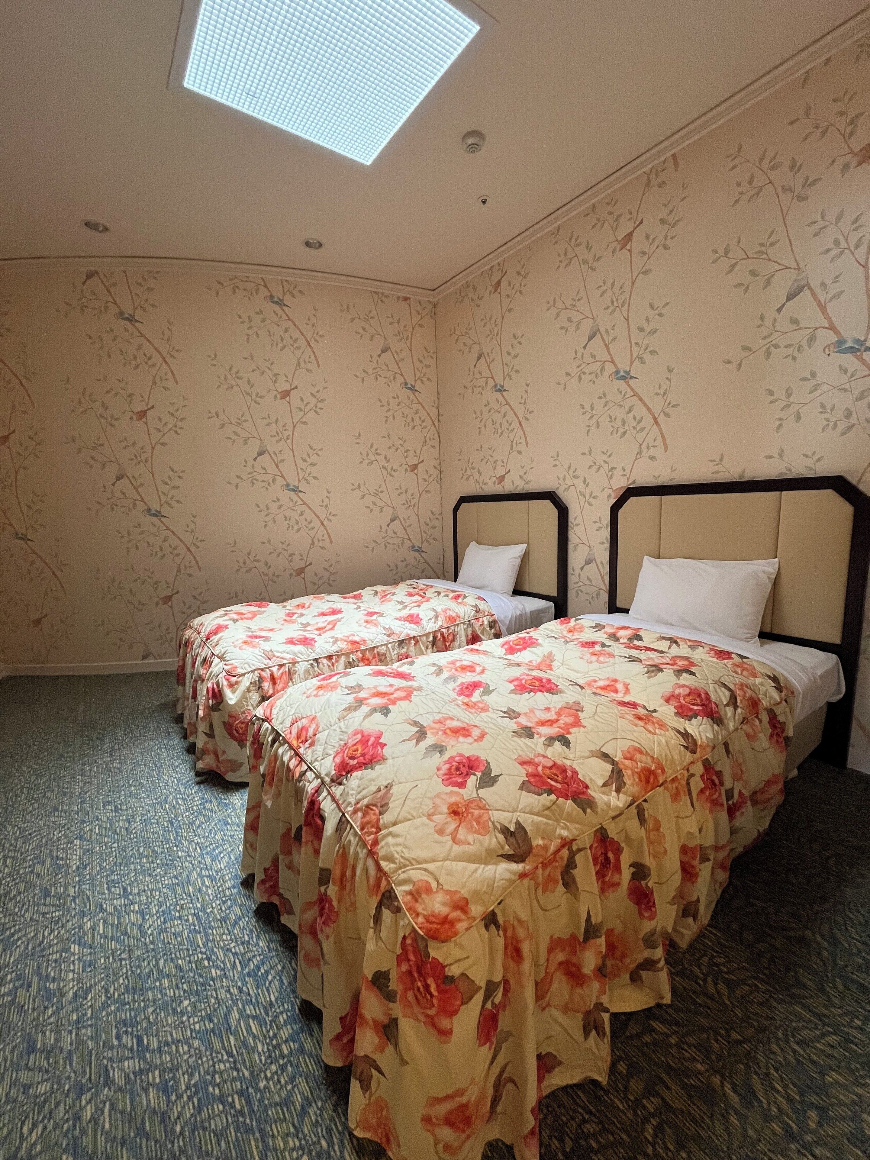 A room with two beds, floral-patterned bedding, a skylight, and patterned wallpaper.