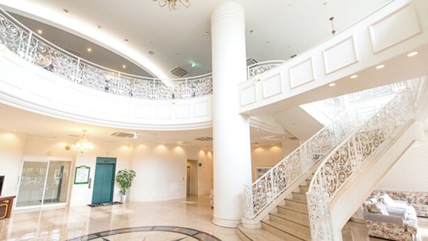 A spacious lobby with a central circular floor design, a grand staircase with intricate railings, and a chandelier.