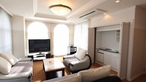 A hotel room with a TV, two sofas, a coffee table, and a kitchenette.