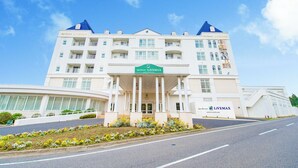 A multi-story hotel with a central entrance, balconies, and a clear sky.