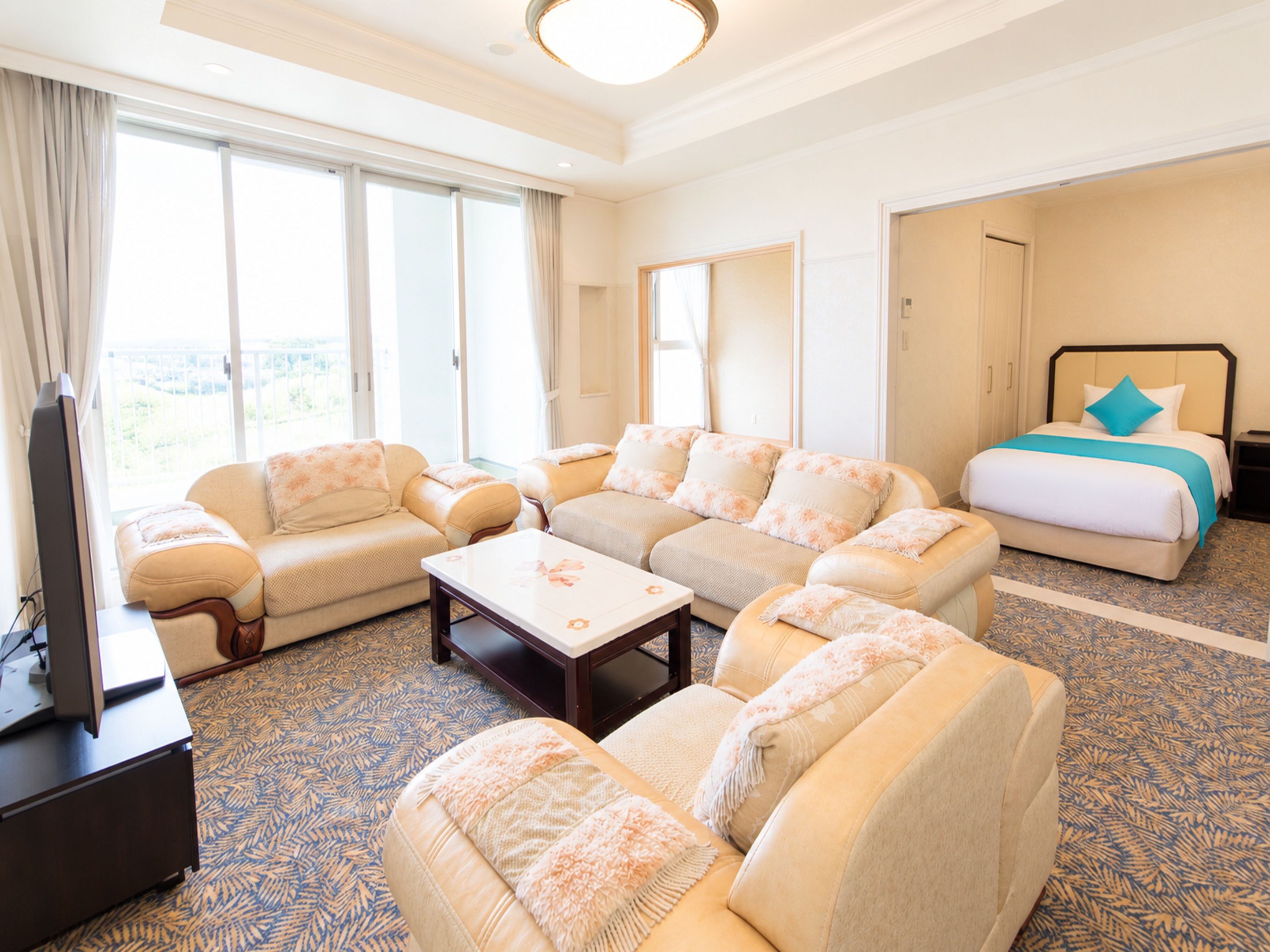 A hotel room with a sofa set, a bed, a television, and a large window.
