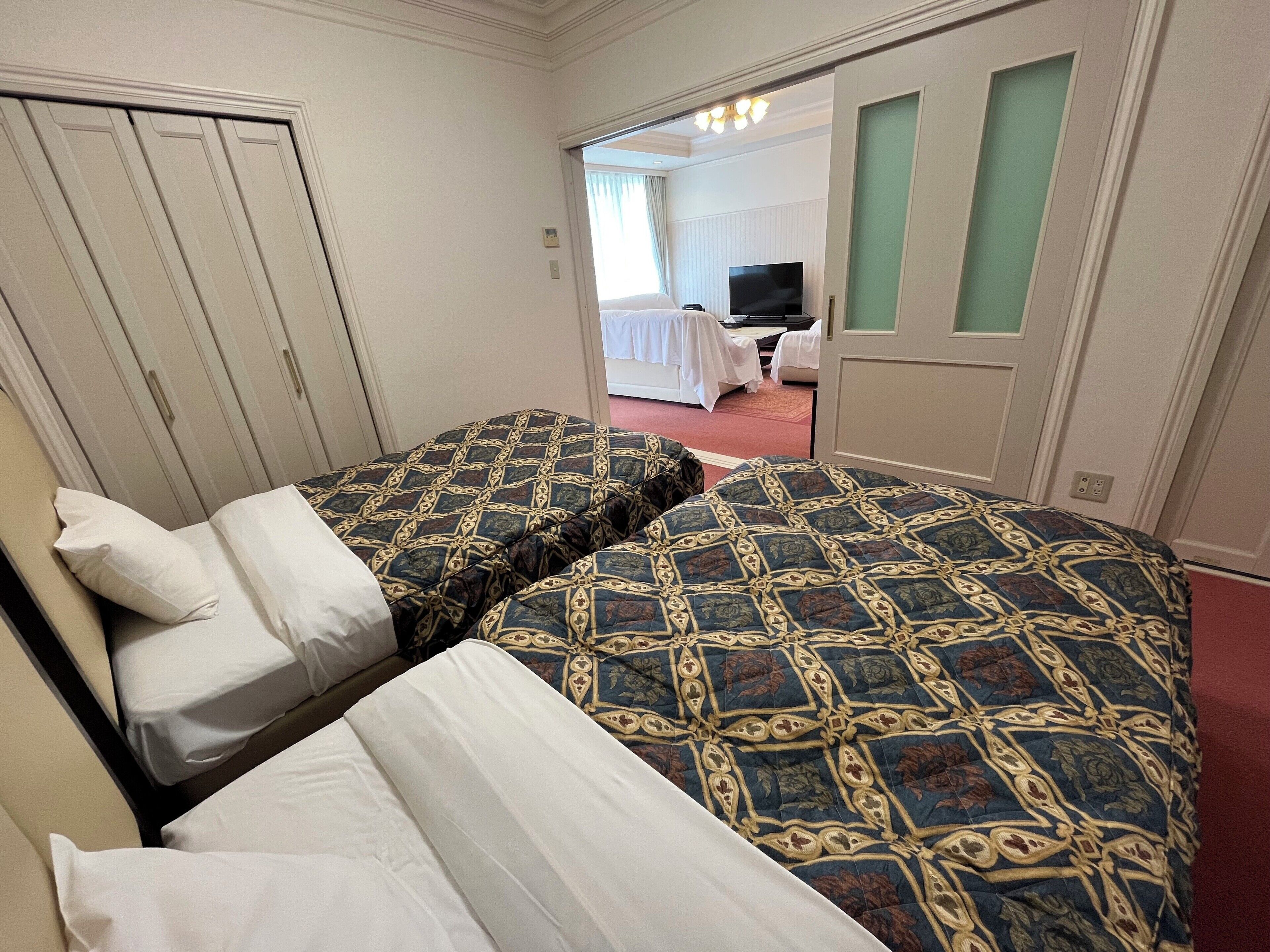 A hotel room with two beds, a television, and a door leading to another room.
