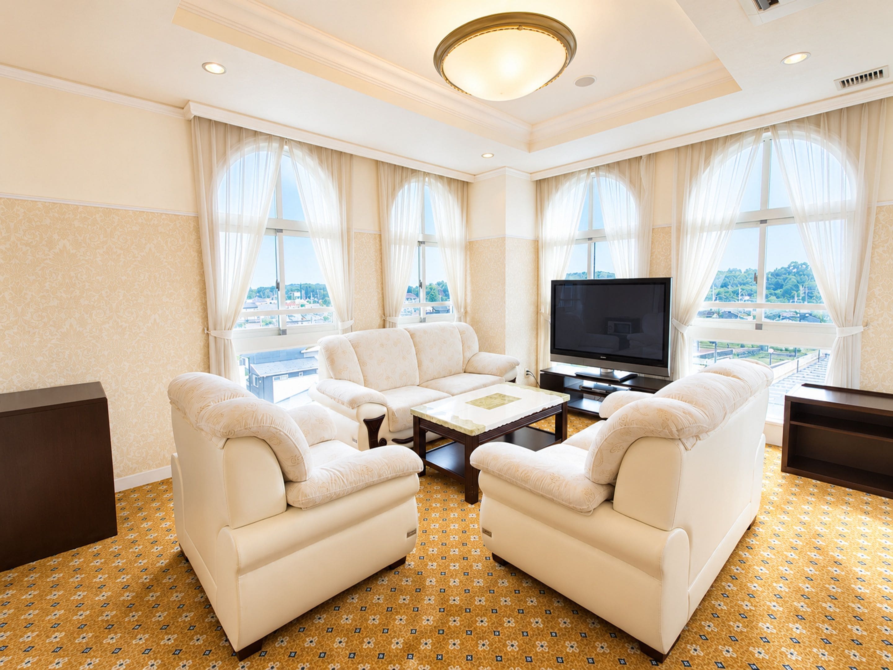 A hotel room with a sofa set, a flat-screen TV, and a large window with a city view.