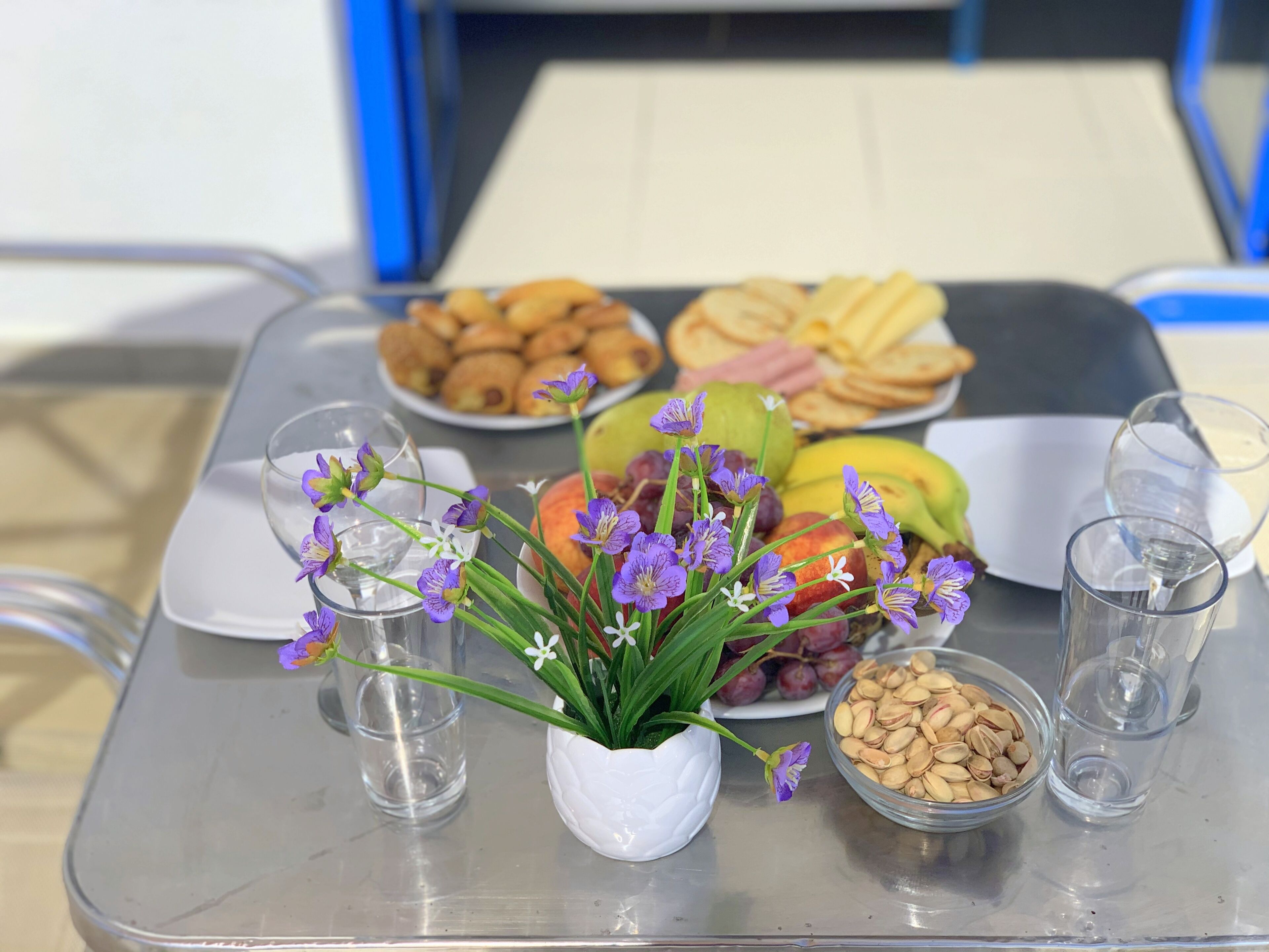 Een tafel met diverse soorten eten, een vaas met paarse bloemen en twee glaasjes water.