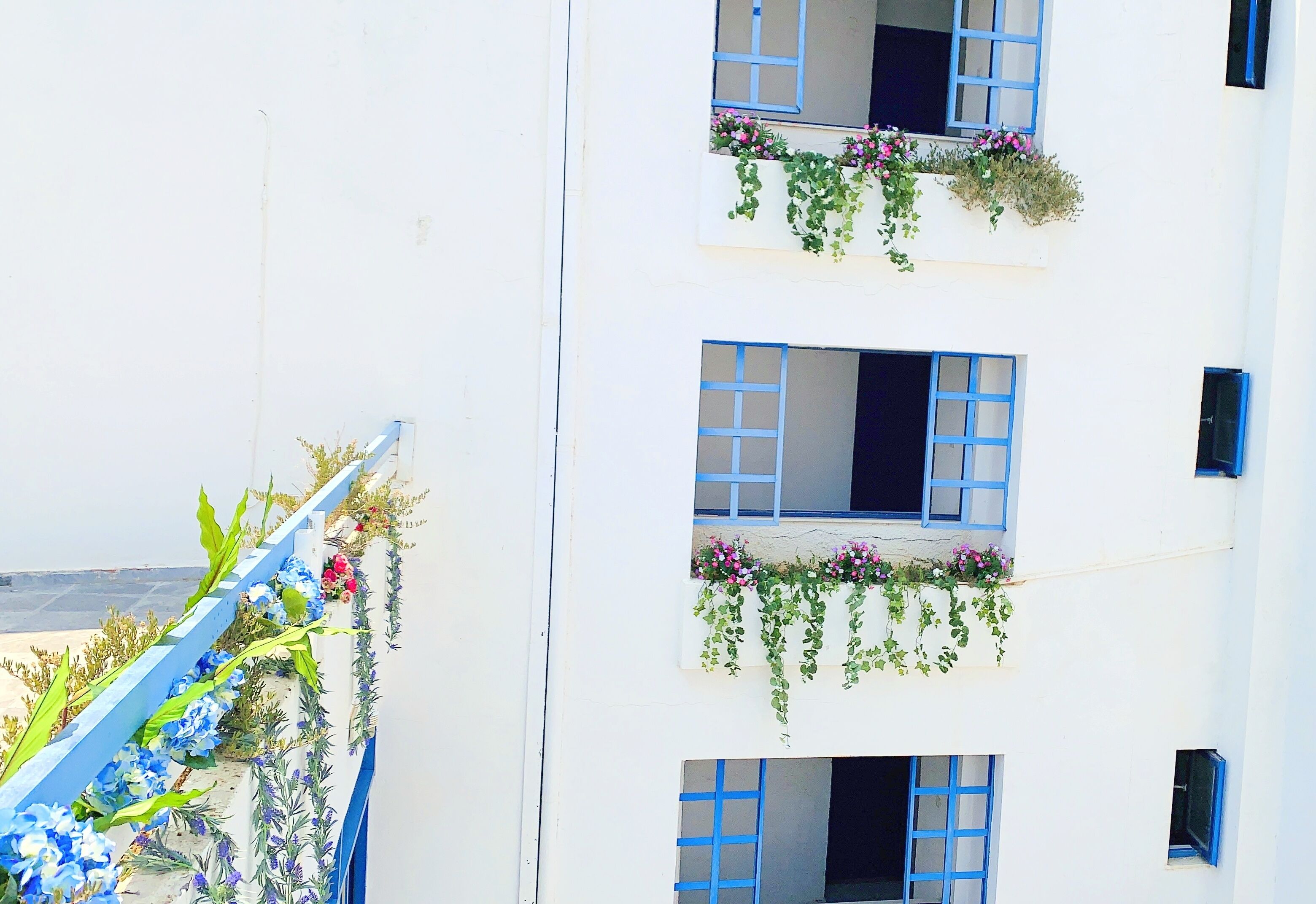 A white building with blue shutters and flower boxes on the balconies.