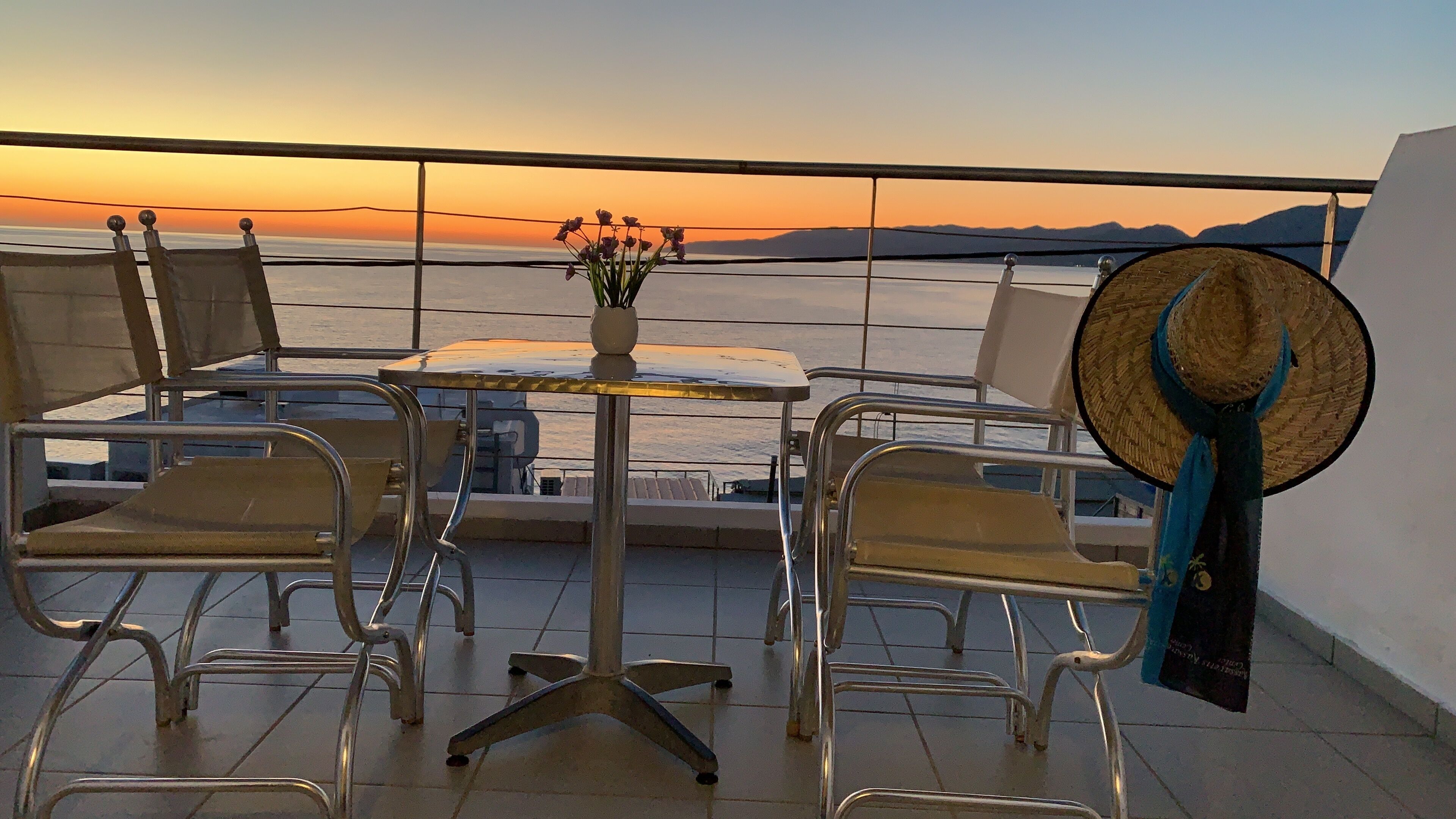 A balcony with a table, chairs, a potted plant, and a straw hat.