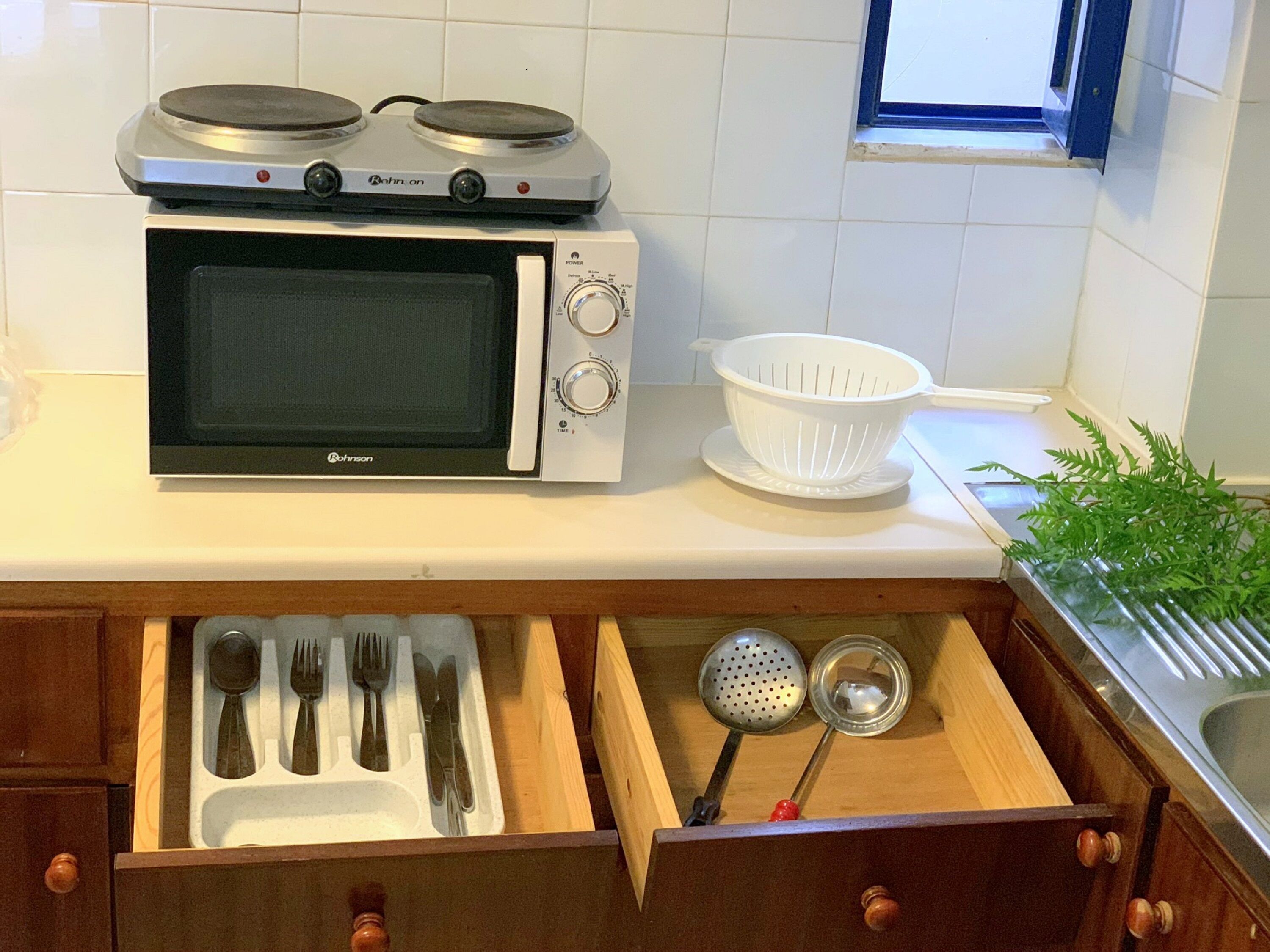 Et køkken med en mikrobølgeovn, en sigte og en skuffe med redskaber.